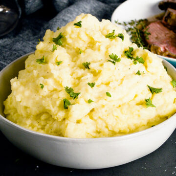 Creamy garlic mashed potatoes piled high in a white bowl with chives on top