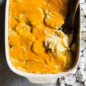 Scalloped potatoes in a baking dish with a wooden spoon