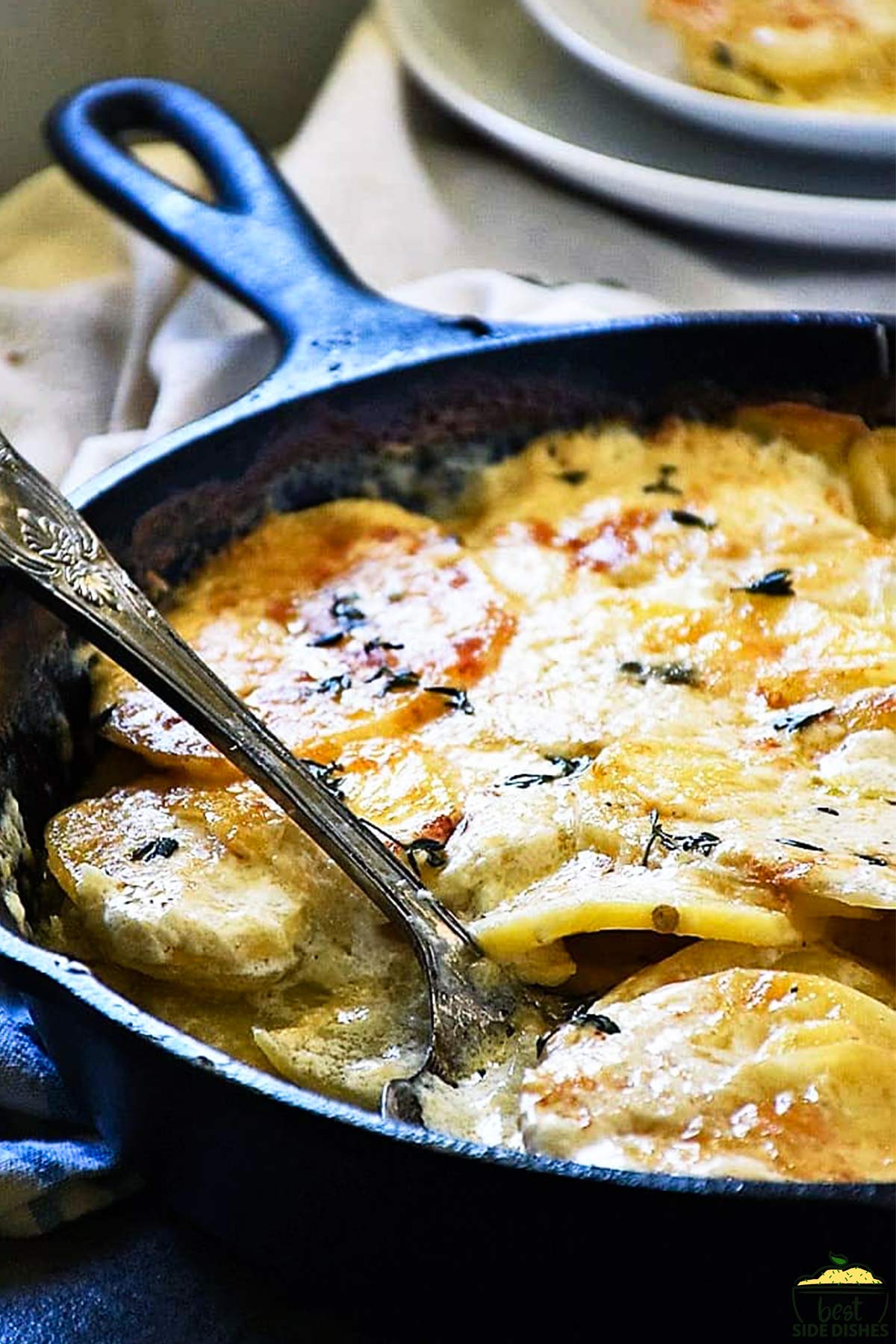 A cast iron skillet of au gratin potatoes with a spoon