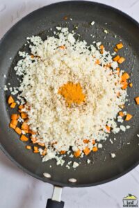 Adding riced cauliflower and seasoning to the pan with the carrots