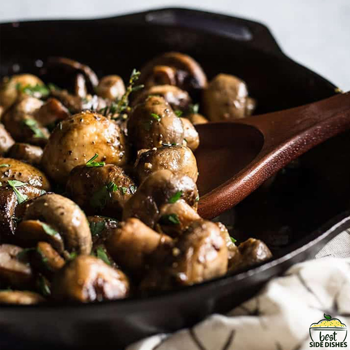 sauteed garlic mushrooms in a skillet with a wooden spoon