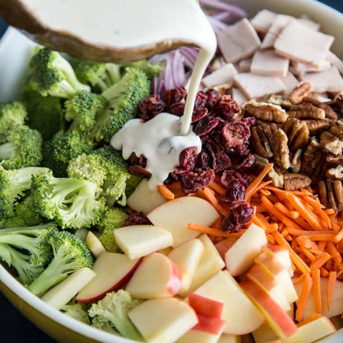 Pouring dressing over broccoli salad with apples