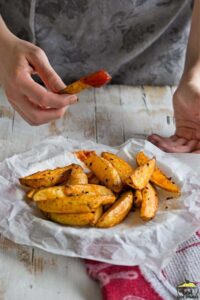Potato wedge dipped in ketchup over plate of potato wedges