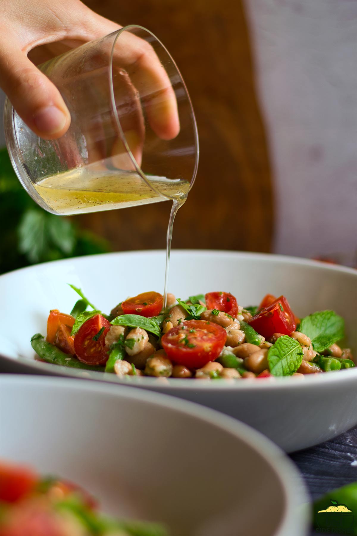 pouring vinaigrette over bean salad in a bowl