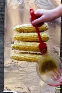 brushing corn cobs with butter on foil