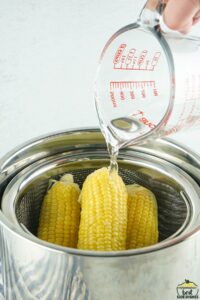 Pouring water into Instant Pot with corn on the cob