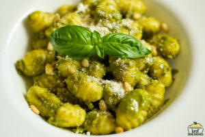pesto gnocchi in a white bowl with a piece of basil on top
