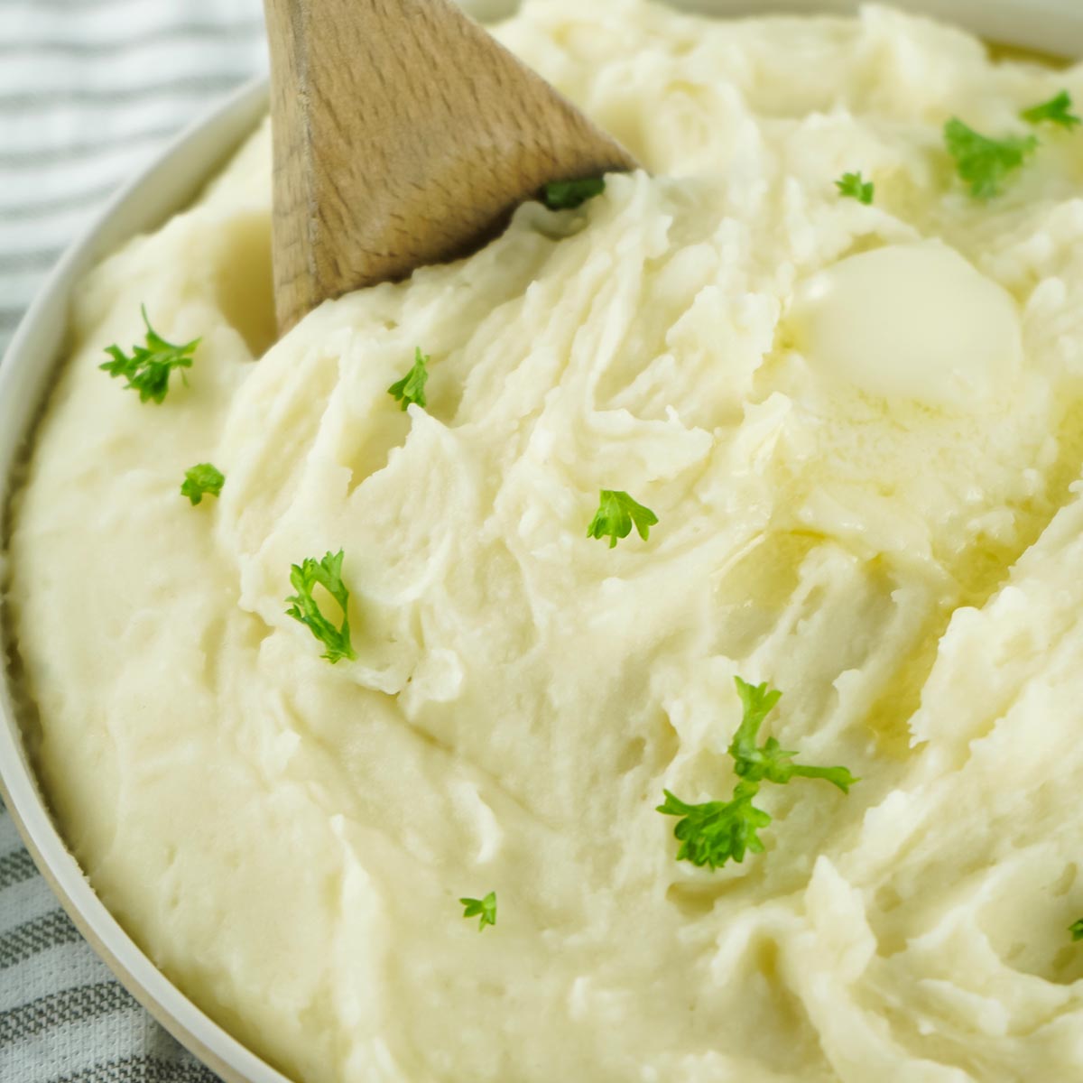 a serving bowl of completed mashed potatoes with a wooden spoon lifting some out