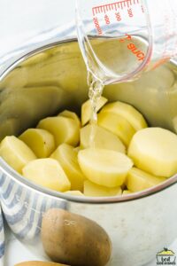 water being poured into a pot full of peeled and sliced potatoes
