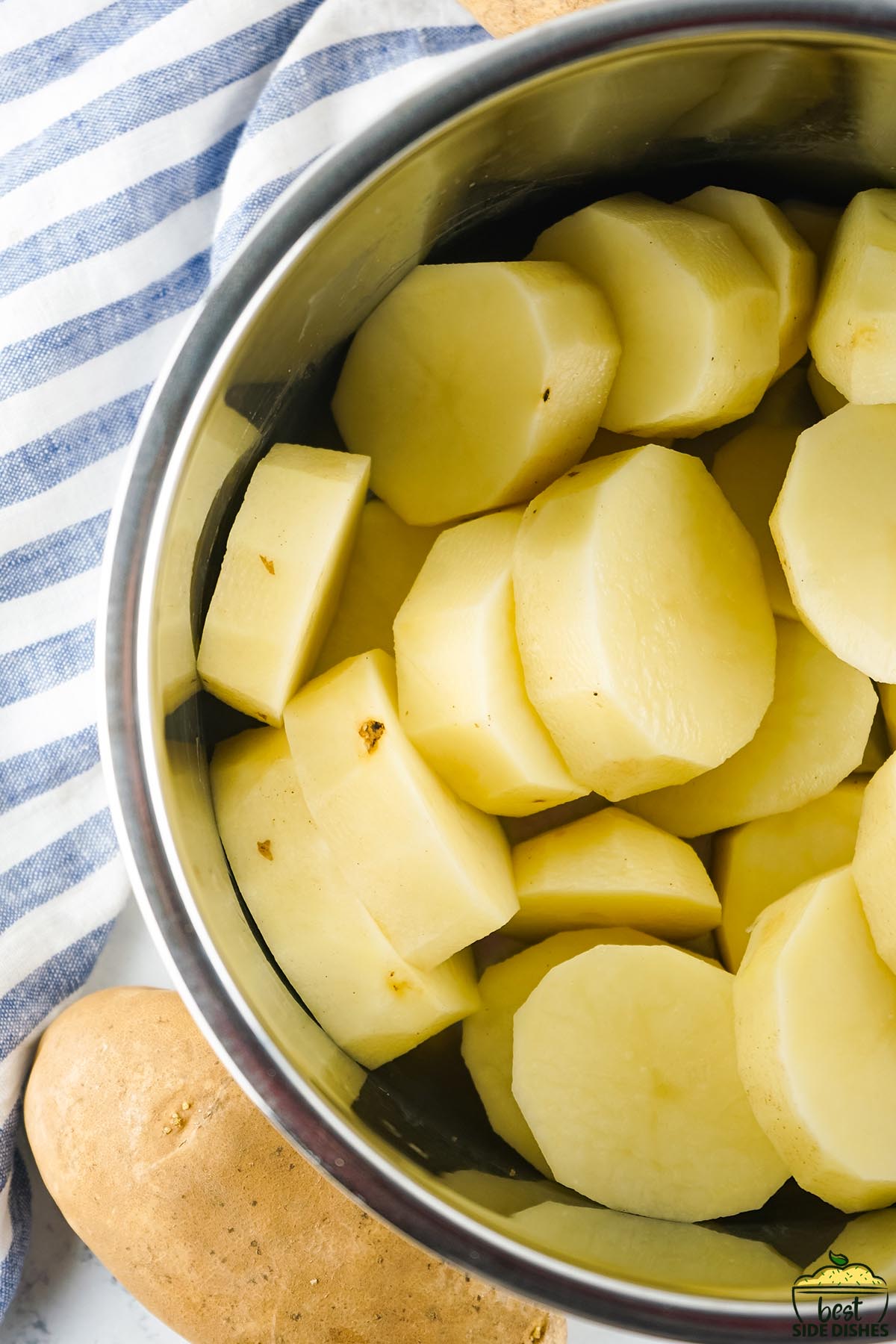 sliced and peeled potatoes in the instant pot next to a whole potato and a tea towel