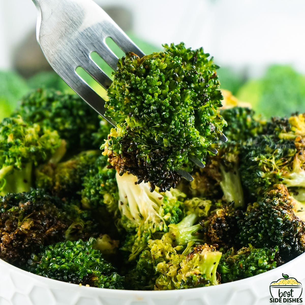 a closeup of a fork holding broccoli over a dish of cooked broccoli