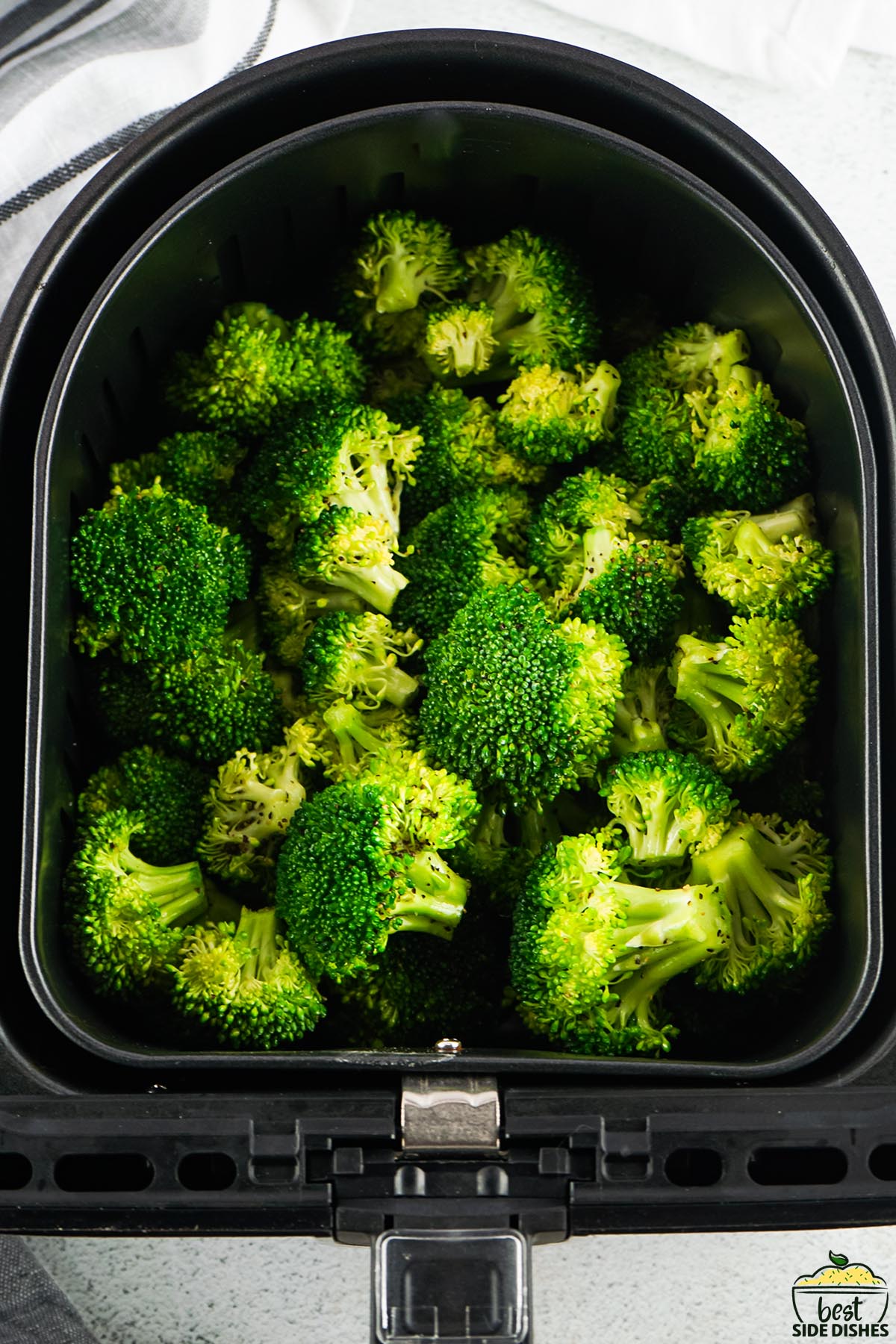 broccoli coated in oil and seasonings in an air fryer basket