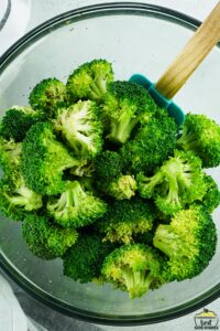 broccoli being mixed with a spatula in a glass bowl