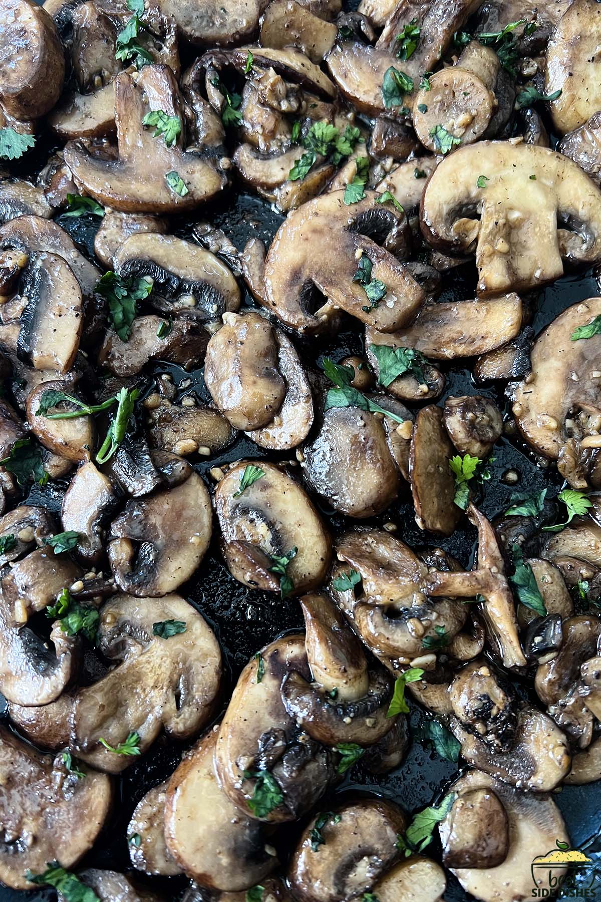 sauteed garlic mushrooms up close in the pan with parsley on top